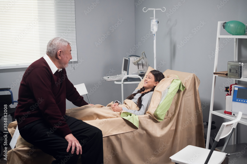 Obraz premium An old man is talking to a girl in a hospital, the girl is staying in bed and smiling cheerfully.