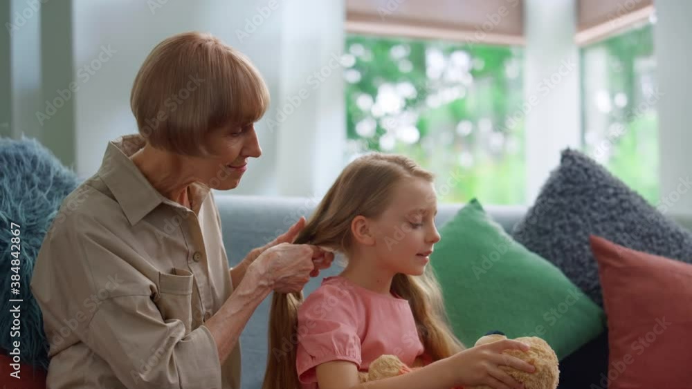 Joyful grandmother braiding little granddaughter hair at living room. Joyful grandmother braiding little granddaughter hair at living room.