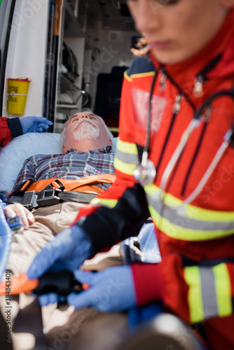 Selective focus of senior man lying on stretcher near paramedics and ambulance car
