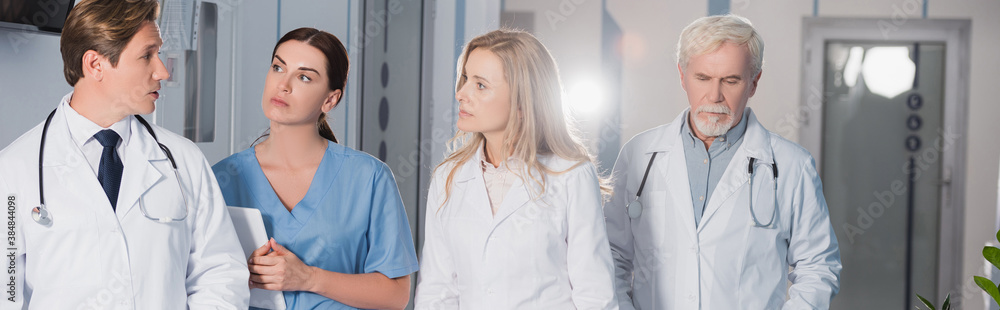 Panoramic shot of doctor talking to colleagues and nurse with digital tablet in hospital Panoramic shot of doctor talking to colleagues and nurse with digital tablet in hospital