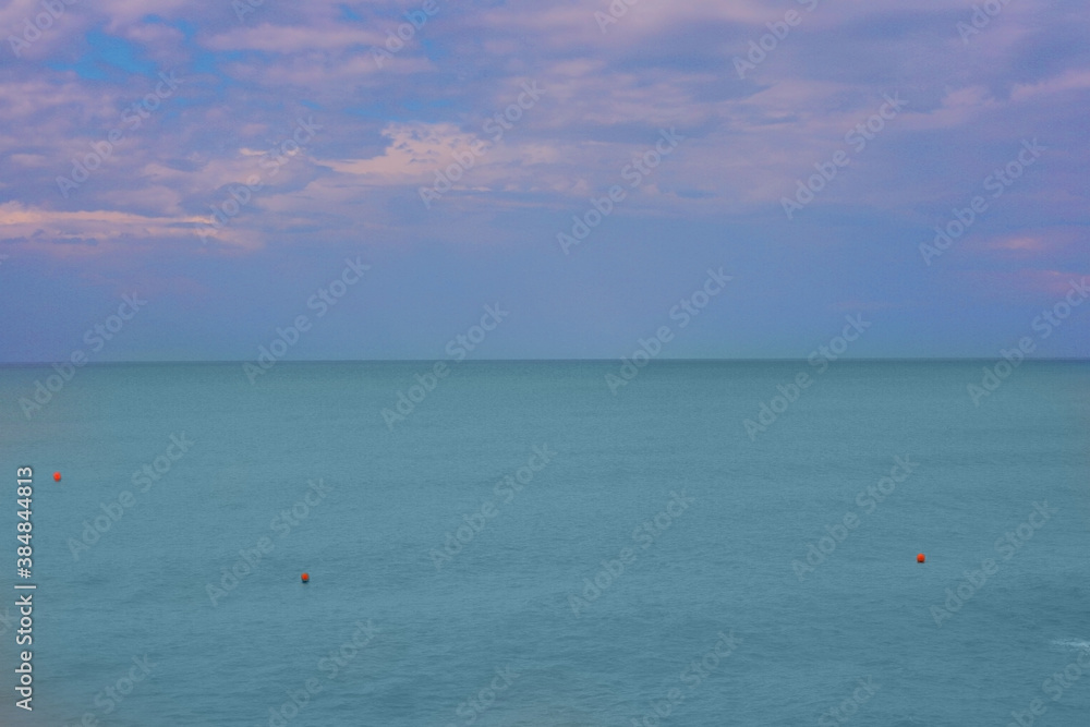 Blurred natural background of blue sky with clouds at sunset and azure sea water with buoys. Copy space.