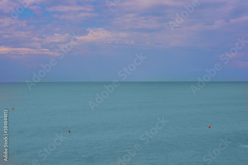 Blurred natural background of blue sky with clouds at sunset and azure sea water with buoys. Copy space. © Ekaterina