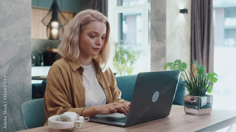 Blond young woman sitting using laptop notebook typing message. Social media studying or working online at home. Slow motion Blond young woman sitting using laptop notebook typing message. Social media studying or working online at home. Slow motion