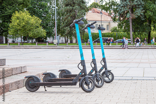 three electric scooters are standing on the city square and waiting for customers