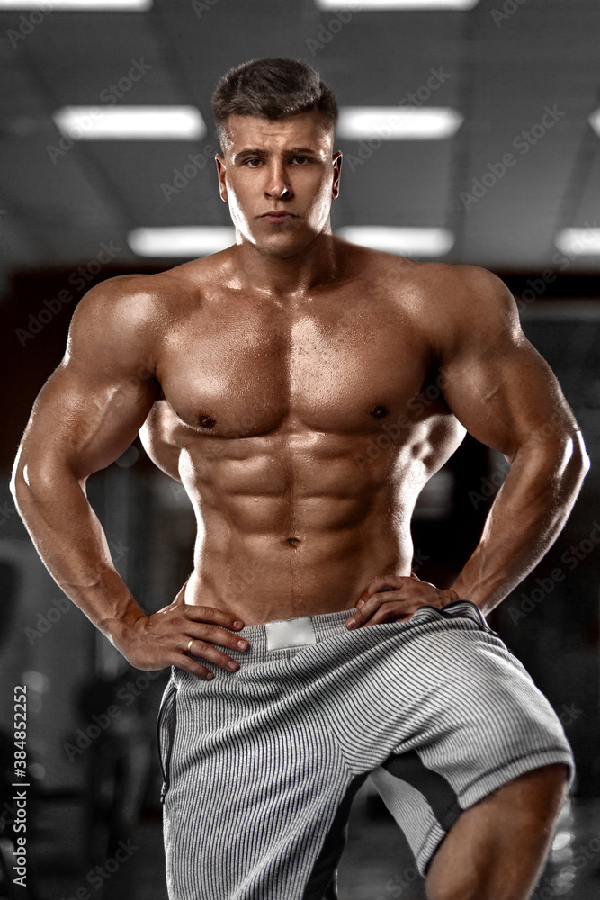 Fototapeta premium Bodybuilder athlet man pumping up muscles in the gym. Brutal strong muscular guy on fitness workout. Bodybuilding concept.
