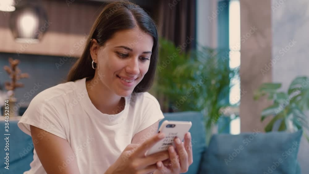 Caucasian attractive nice happy woman with smartphone smiling when reading messages on social media sitting on couch indoors. Stylish interiors. Casual lifestyle. Modern people. Caucasian attractive nice happy woman with smartphone smiling when reading messages on social media sitting on couch indoors. Stylish interiors. Casual lifestyle. Modern people.