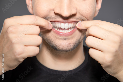 Tableau sur toile man apply whitening strip on his teeth by hands while smiling into camera
