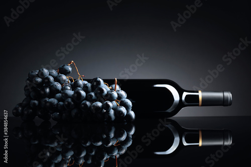 Bottle of red wine and a bunch of grapes on a black reflective background. © Igor Normann