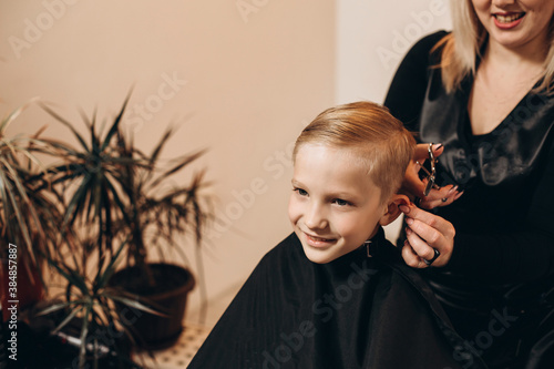 Eight-year-old blonde boy at the barbershop. A hairdresser cuts a haircut at a home beauty salon. Selective focus.