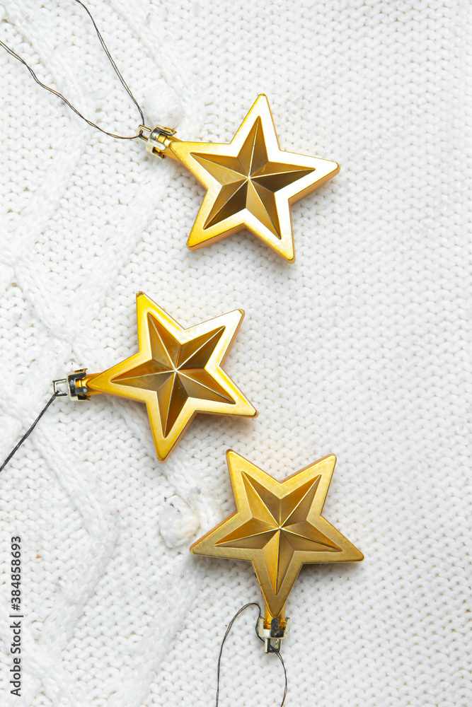 Fototapeta premium Christmas toys stars are Golden . Golden Christmas toys. White knitted fabric. New year and Christmas holidays. Christmas layout on top. Article about the holiday.