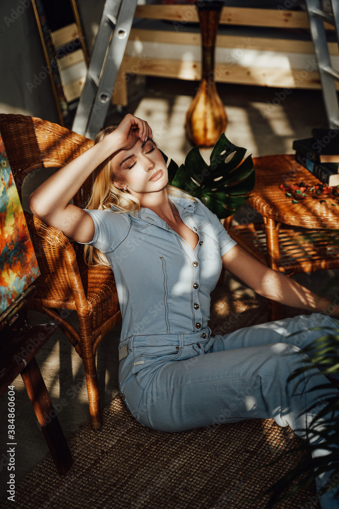 Glamour blond dressed in styled jeans clothes napping lying on bamboo carpet around wooden furniture in room in shadows and sunshine.
