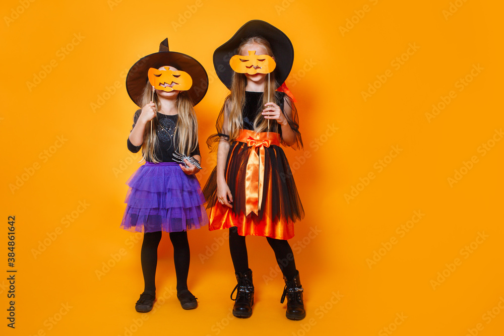 Obraz premium Two little girls in halloween costumes having fun with pumpkin on orange background