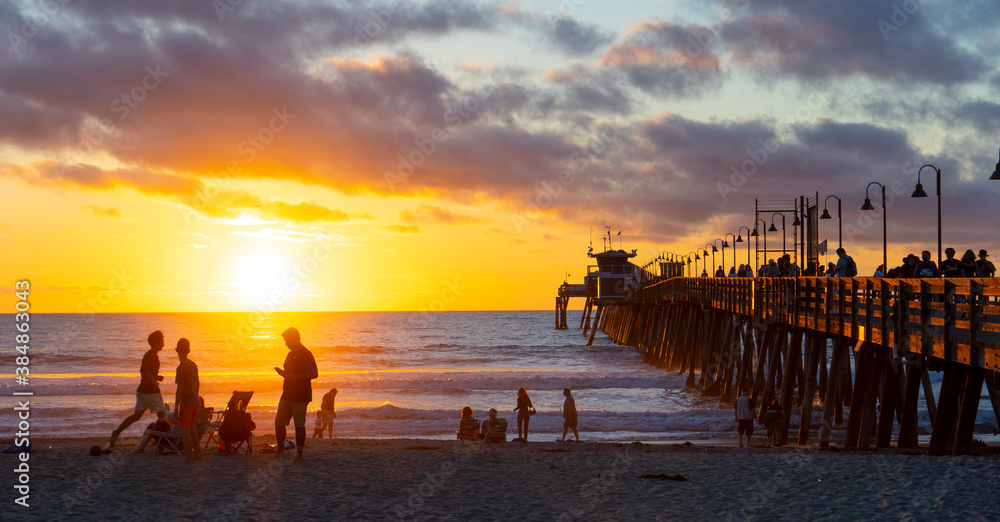 Naklejka premium Pier at sunset with people on the beach