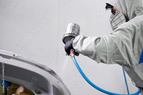 young caucasian auto mechanic is engaged in car painting details in automotive manufacturing industry, use machine equipment © Roman