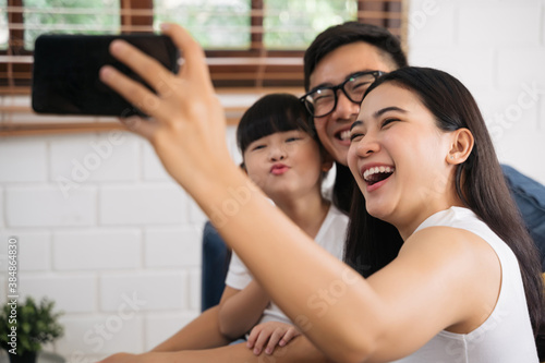 Happy family taking a selfie, smiling at a phone in their house. Young asian mother is taking selfie of her family smiling.