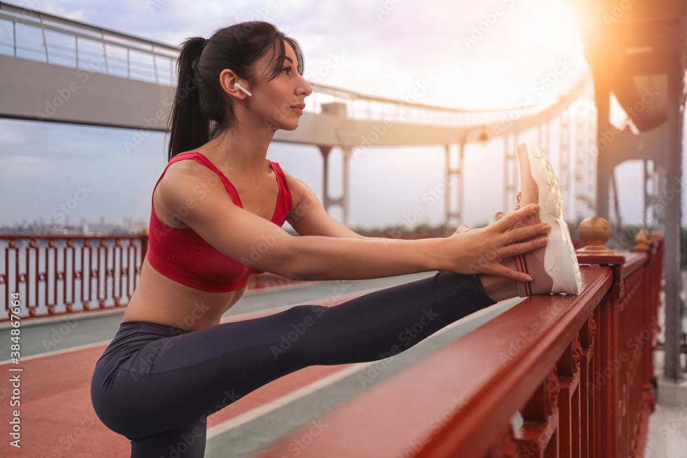 Cheerful young woman working out legs flexibility before training in the city