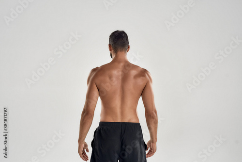 Rear view of muscular man with naked posing isolated over grey background, studio shot