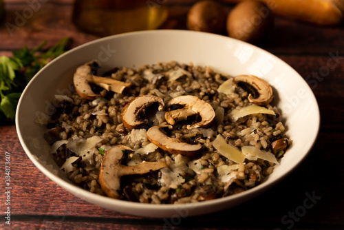 mushroom risotto, italian food known as "risotto ai funghi", closeup with warm light, parsley, side view, on dark brown wooden table. parmesan flakes and olive oil.
