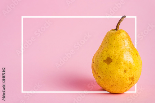 Fresh yellow ripe pear on pink background with white frame copy space