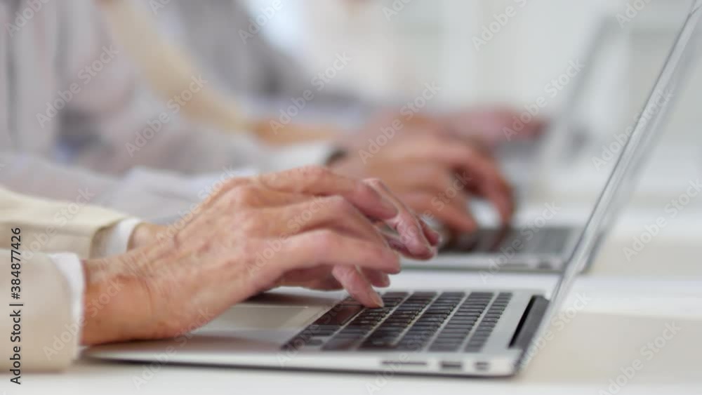 Sequence of shots of cheerful senior men and women with grey hair sitting at desks and using laptops in computer class as male middle-aged teacher with beard monitoring their progress and helping Sequence of shots of cheerful senior men and women with grey hair sitting at desks and using laptops in computer class as male middle-aged teacher with beard monitoring their progress and helping