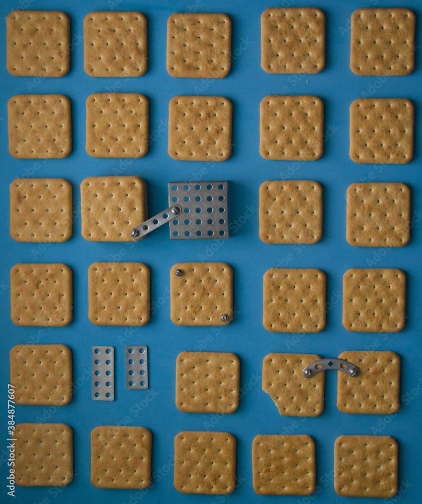 Crackers and constructor details on a blue background. Nuts and screws. Synesthesia. Iron cookie. An edible puzzle. High quality photo. Conceptual still life. Product photography. Different objects Crackers and constructor details on a blue background. Nuts and screws. Synesthesia. Iron cookie. An edible puzzle. High quality photo. Conceptual still life. Product photography. Different objects