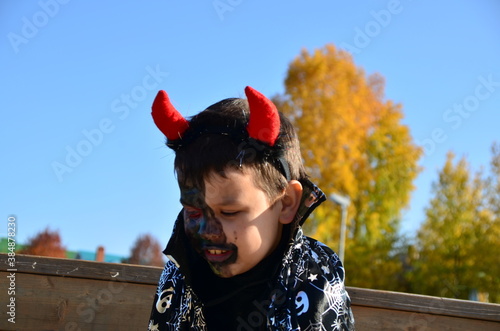 funny baby in devil halloween costume with horns and trident on a dark wooden background boy with black makeup for halloween  zombie