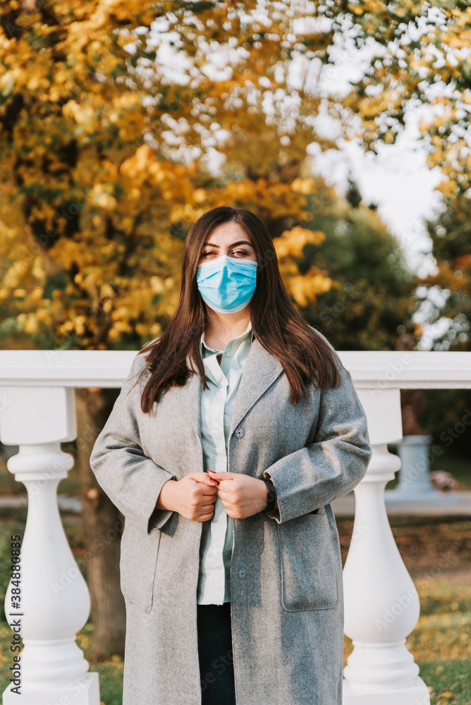 Portrait of a beautiful adult young woman on the background of autumn in the Park in a medical face mask