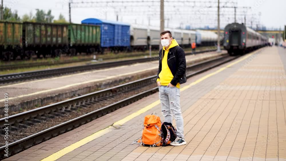 custom made wallpaper toronto digitalYoung man in medical mask stands on platform, waiting for train. Male passenger in protective mask with backpacks on railroad platform in waiting for train ride during coronavirus pandemic.