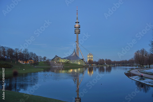 Sunset in the Olympiapark in Munich with view on the lake and tower. Skyscraper behind a lake in the city. © loopzn