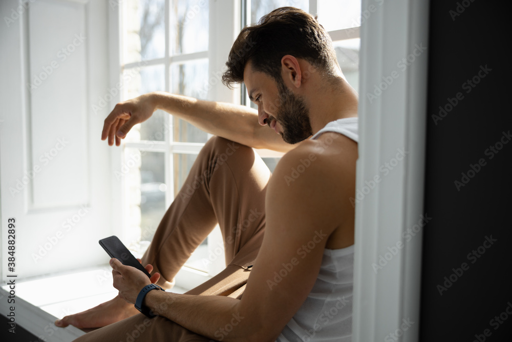 Cropped shot of man sitting on windowsill with mobile phone