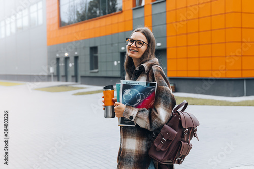 Portrait of girl student standing at university campus. Laughing Woman wearing braces, eyeglasses, bag with books having coffee break after lecture. Enjoying College life. Learning education concept.