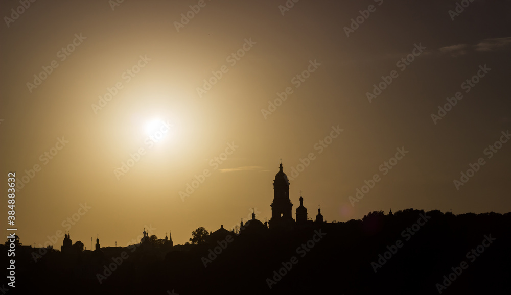 Silhouettes of churches in the setting rays of the summer sun. Contrasting background with black and gold hues.