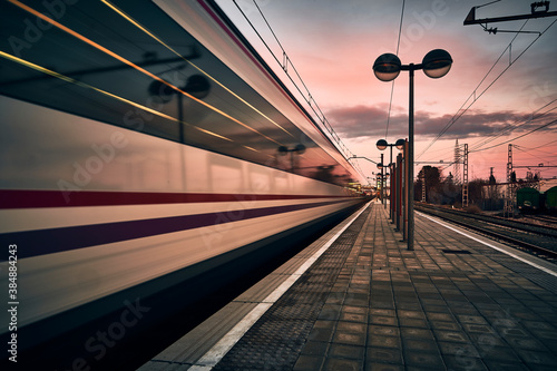 tren de cercanias pasando a velocidad fugaz al atardecer en una estacion de tren con farolas photo