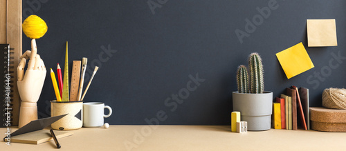 Creative desk with notebook, desk objects, office supplies, books, and cactus on a dark blue background.	
 photo