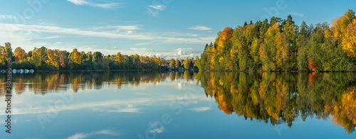 Panorama view of autumn colored trees in sunlight, along the riverbank of the...