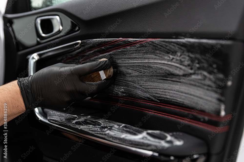Car detailing studio worker cleaning leather car interior upholster