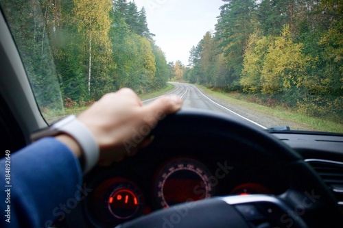 Driver is driving on the road in the forest, holding the wheel with hand. View from the car.