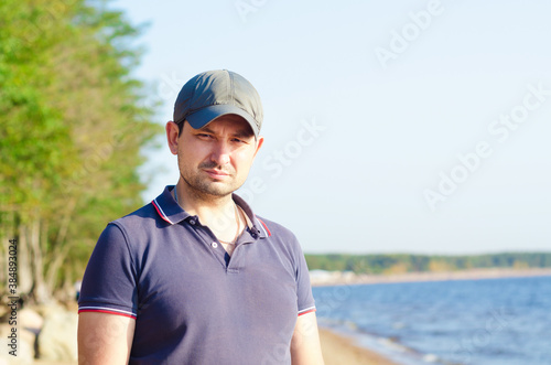 Portrait of handsome young man in cap with a light bristle against the sea beach in summer looking at the camera. © Елена Якимова