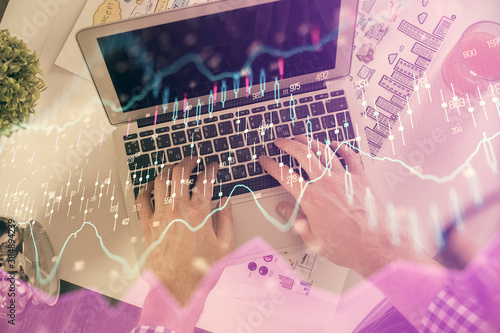 Double exposure of man's hands typing over laptop keyboard and forex chart hologram drawing. Top view. Financial markets concept.