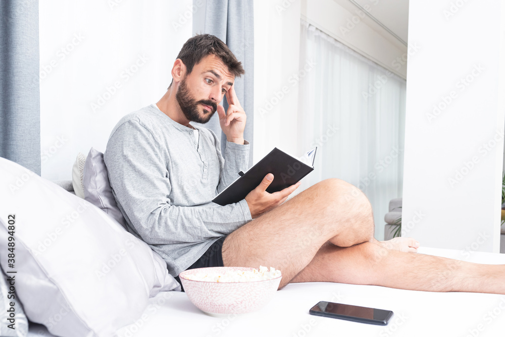 Anxious man reading a book on bed at home Anxious man reading a book on bed at home