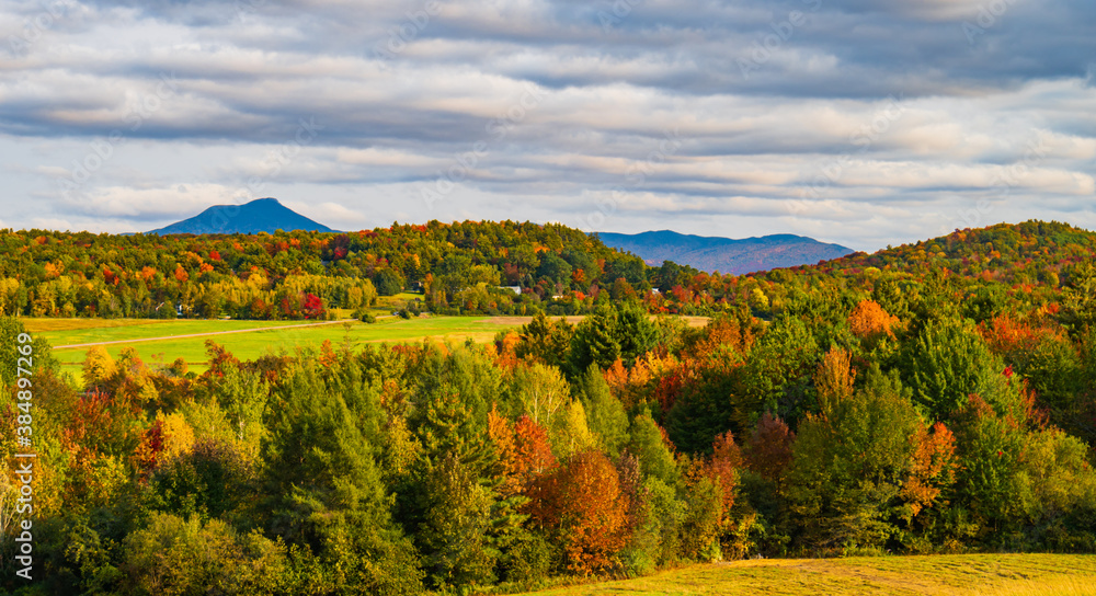 view of rural farm fields and forests  with Camels Hump Mountain in fall foliage season, in Vermont
