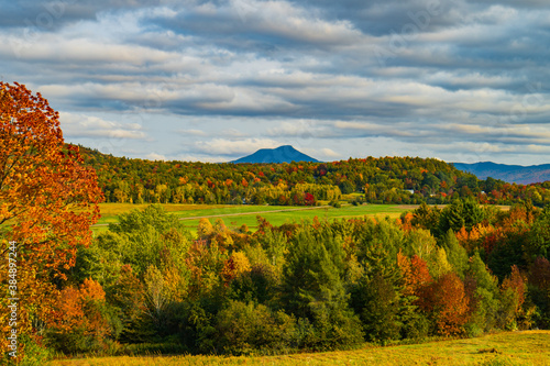 view of rural farm fields and forests with Camels Hump Mountain in fall foliage season, in Vermont 