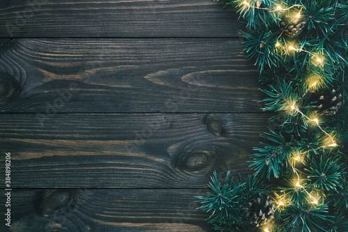 Fir branches and christmas lights on dark wooden background with copy space. Flat lay, top view.