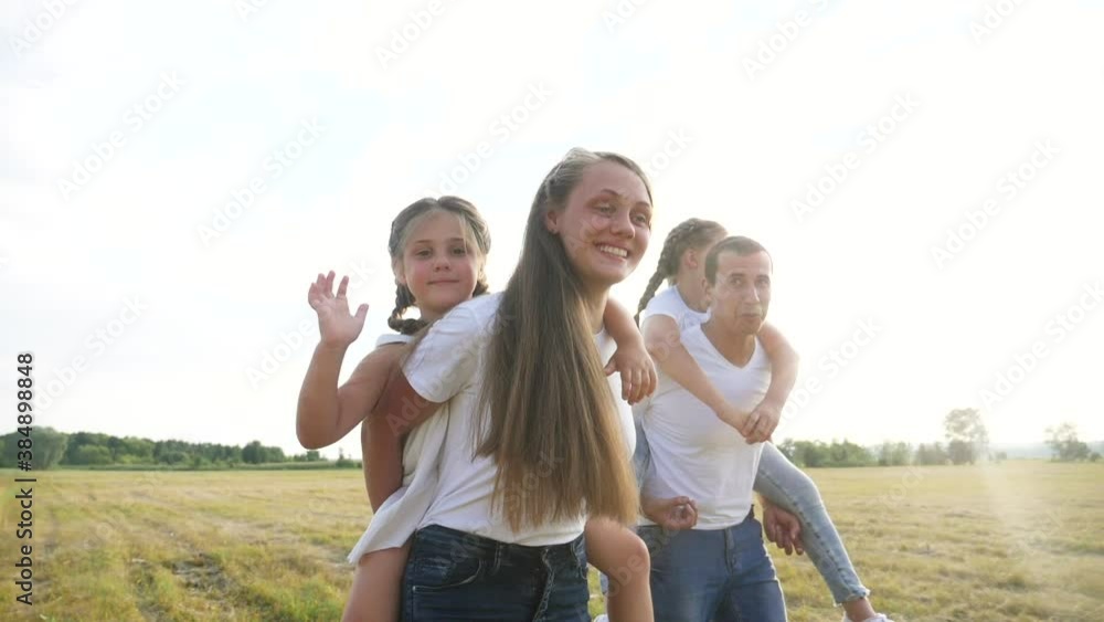 dream holiday concept. happy family fun walks in the park with kid. parent father and mother carry children with sister and daughter on their backs go field. friendly family walks together during dream holiday concept. happy family fun walks in the park with kid. parent father and mother carry children with sister and daughter on their backs go field. friendly family walks together during