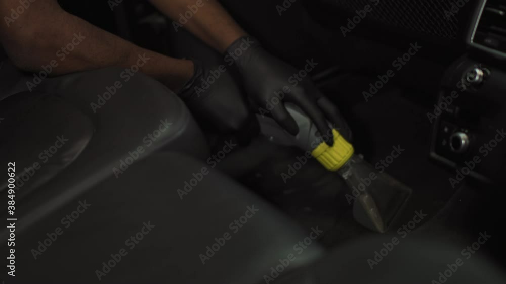 A young African-American cleans the car mat with a special device, work for students. Work at the car wash