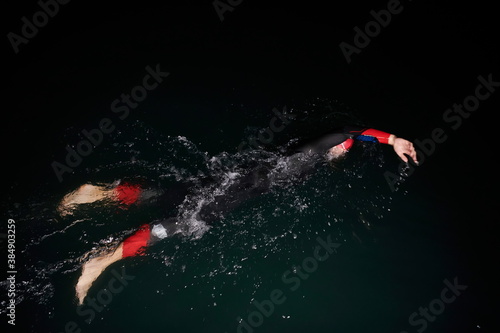 triathlon athlete swimming in dark night wearing wetsuit photo