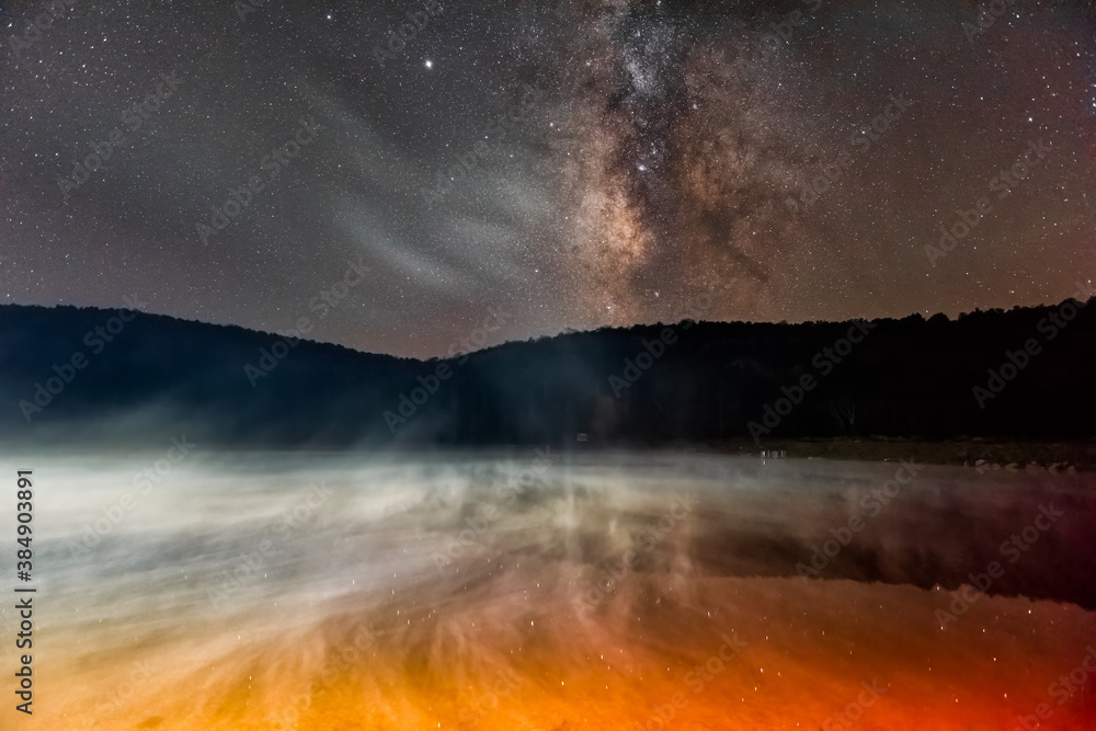 Night dark sky with milky way in Spruce Knob Lake in West Virginia with rising red yellow mist from water and reflection of stars landscape view Night dark sky with milky way in Spruce Knob Lake in West Virginia with rising red yellow mist from water and reflection of stars landscape view