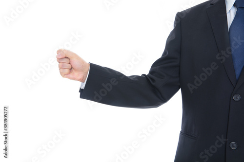 Male in black suit in front of white background makes fist and stretches out hand