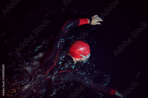 triathlon athlete swimming in dark night wearing wetsuit photo