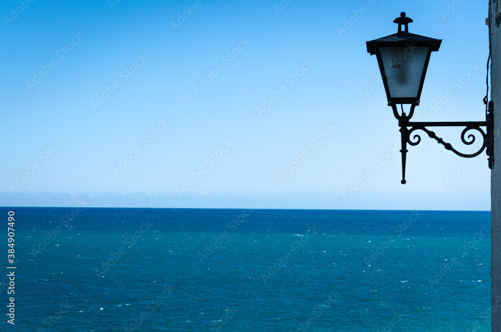 Lamppost on a wall with the turquoise sea water in the background, Peniscola, Castellon, Spain